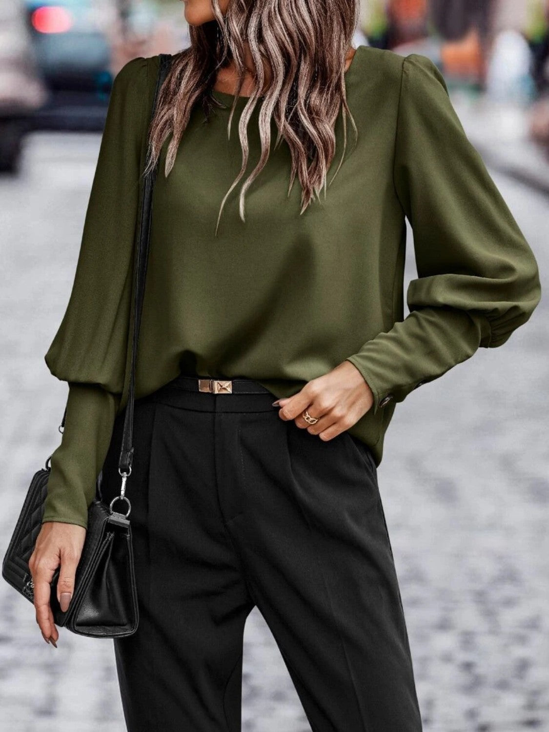 Woman wearing an olive green blouse, black pants, and black handbag on a city street