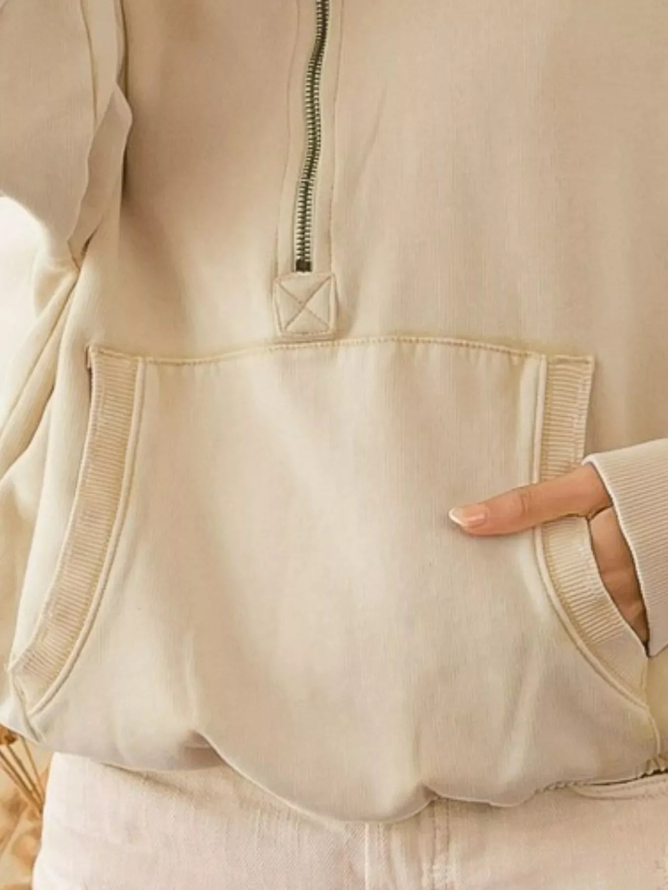 Close-up of beige half-zip hoodie with front kangaroo pocket and hand in pocket