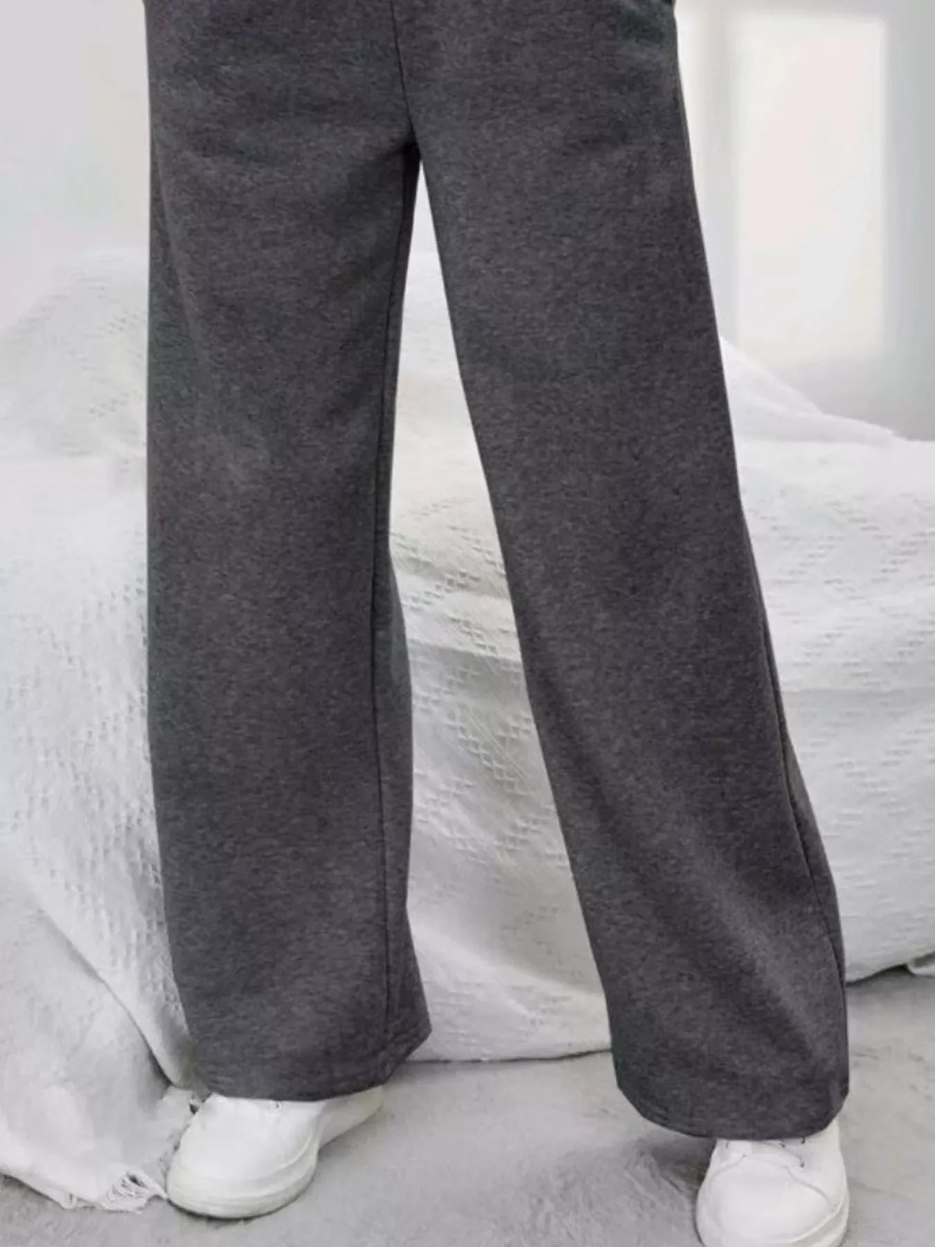 Person wearing loose dark gray sweatpants and white sneakers standing indoors