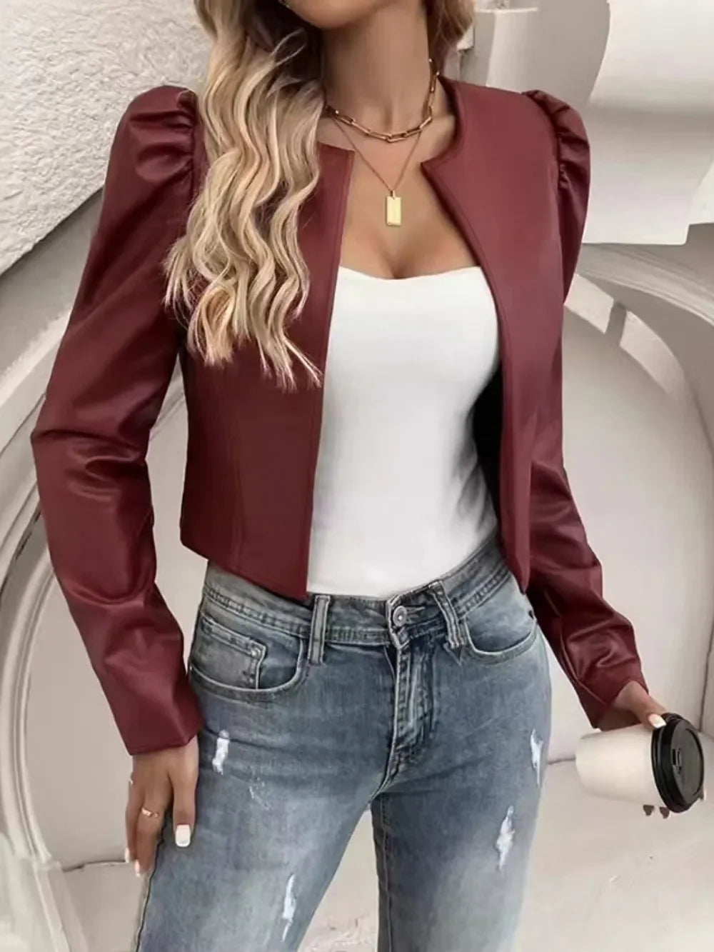 Woman wearing a burgundy faux leather puff sleeve cropped jacket, white top, and blue jeans.
