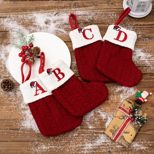 Red knitted Christmas stockings with white cuffs and embroidered letters A, B, C, D on wooden surface with snow and holiday decorations