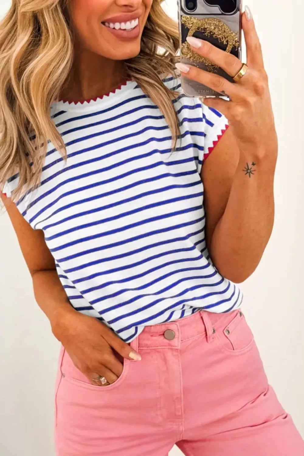 Woman in blue and white striped top with pink jeans, taking mirror selfie