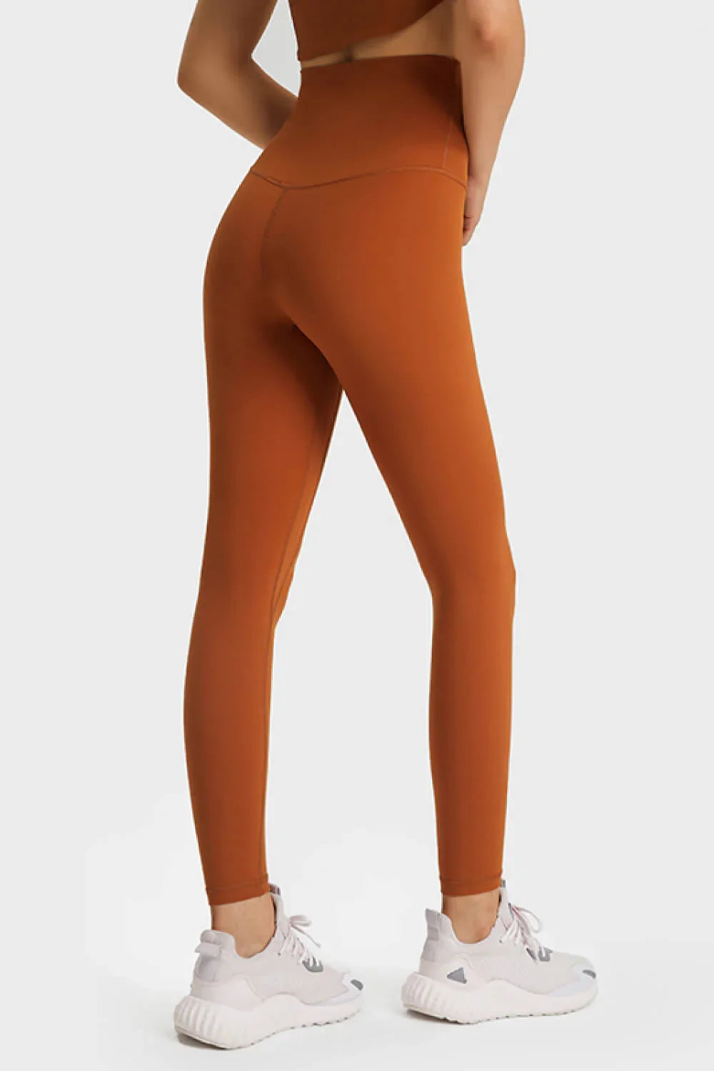 Close-up of woman wearing rust orange high-waisted leggings with white athletic shoes on white background