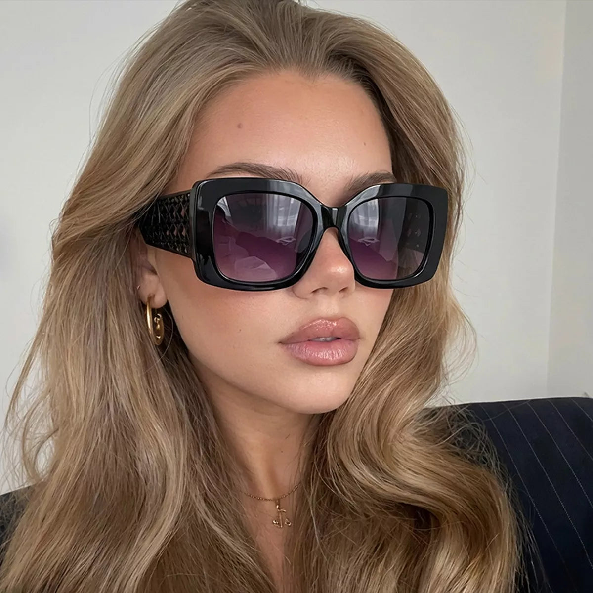 Woman wearing oversized black square sunglasses and gold hoop earrings.