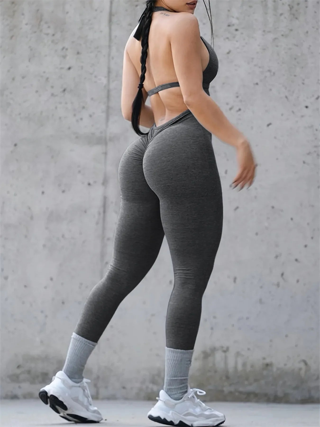 Woman in gray sportswear and white sneakers posing against concrete wall, fitness leggings and crop top
