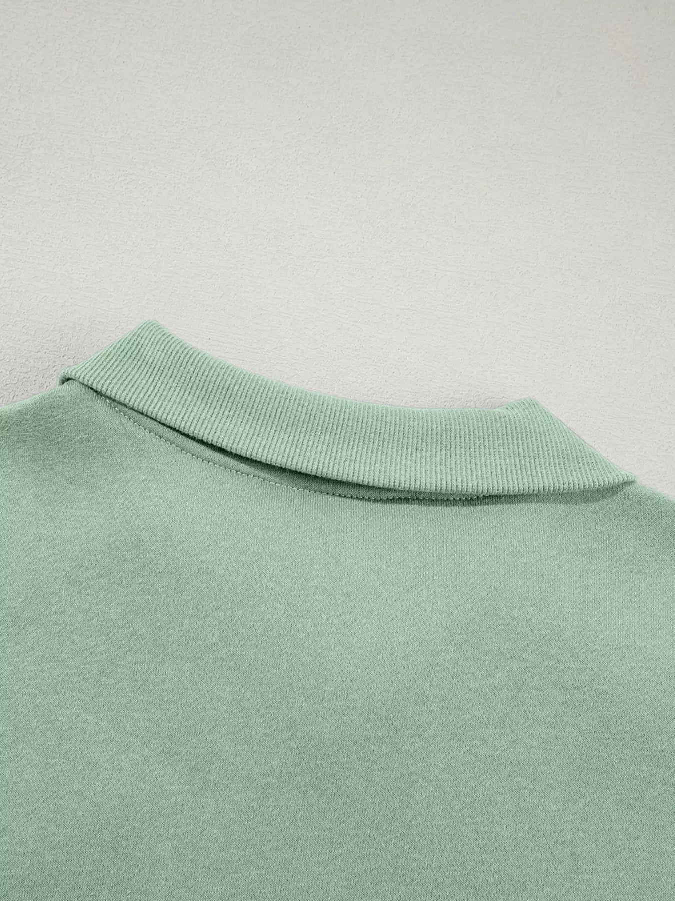 Close-up of a light green knit collar on a soft fabric garment against a textured background