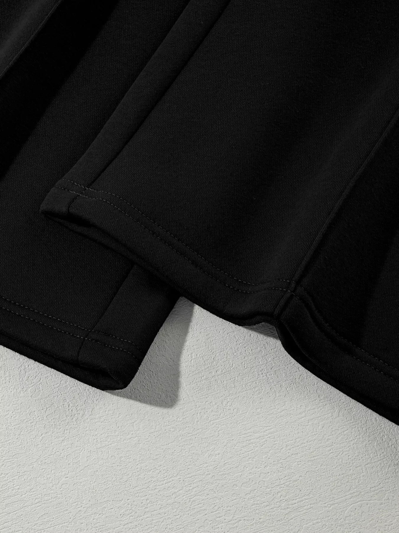 Close-up of black garment hems with double stitching on textured white surface