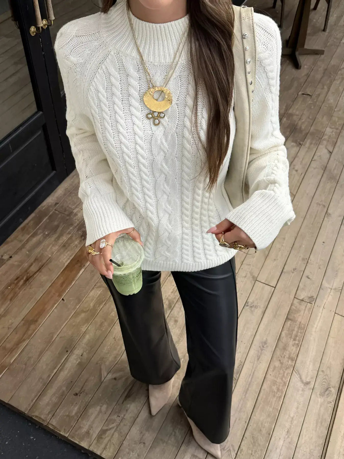 Woman wearing an Evie's Dreamland white mock neck cable-knit sweater with black faux leather pants.