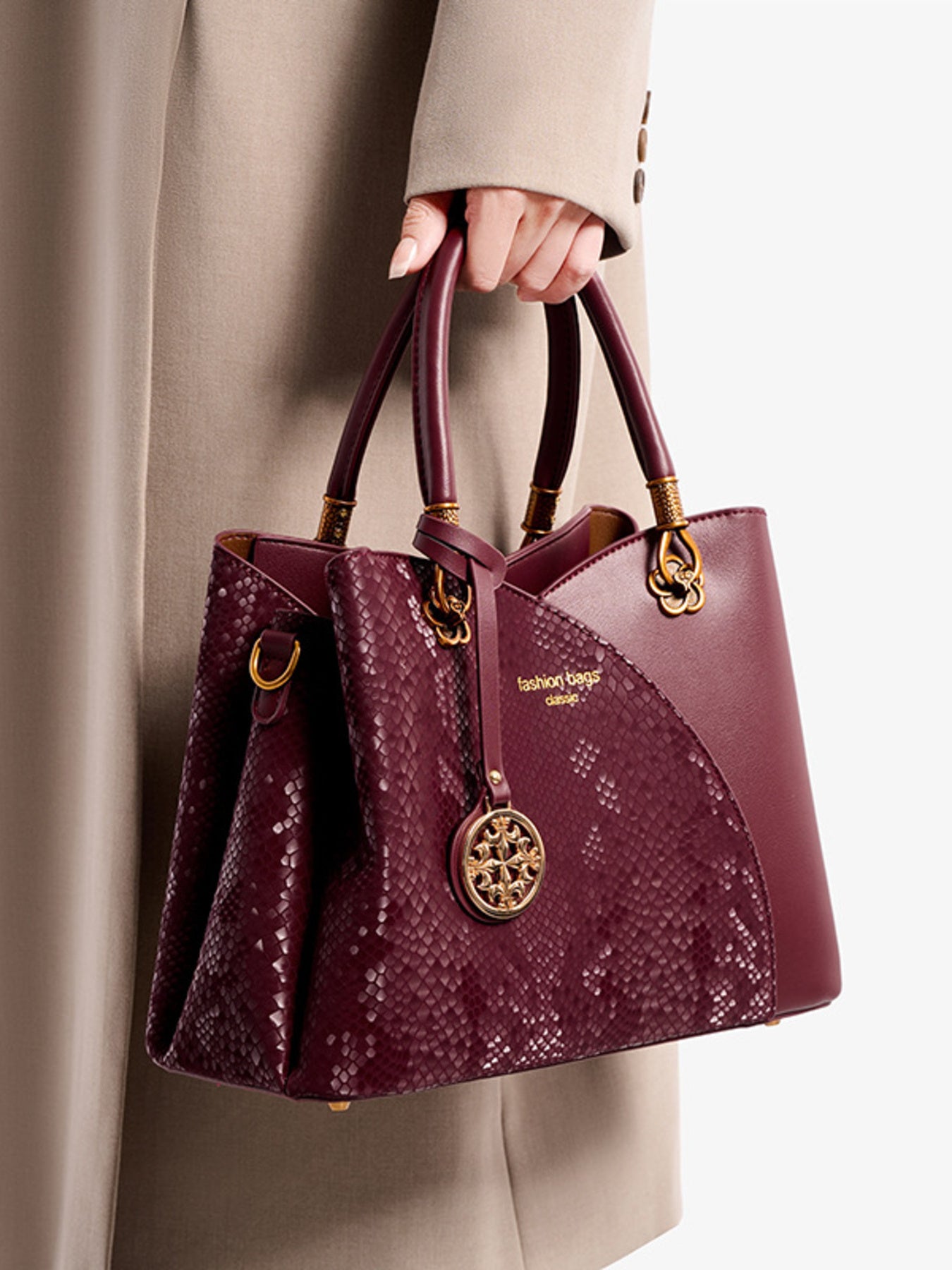 Woman holding burgundy snakeskin tote handbag with gold accents and a stylish charm