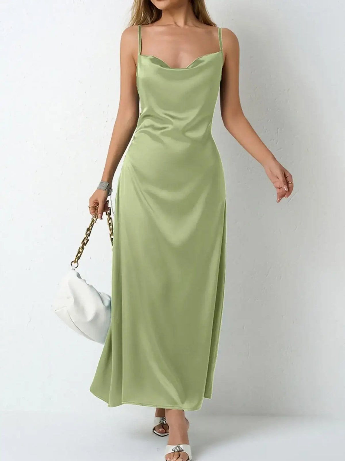 Woman wearing an Evie's Dreamland sage green satin cowl neck slip maxi dress with a white handbag.