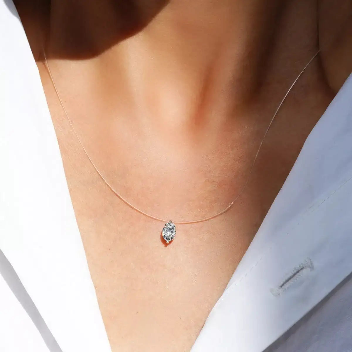 Evie's Dreamland moissanite pendant necklace with an oval stone on a clear cord, worn over a white shirt.