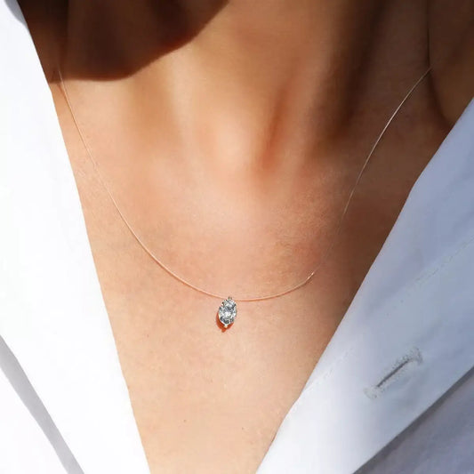 Evie's Dreamland moissanite pendant necklace with an oval stone on a clear cord, worn over a white shirt.