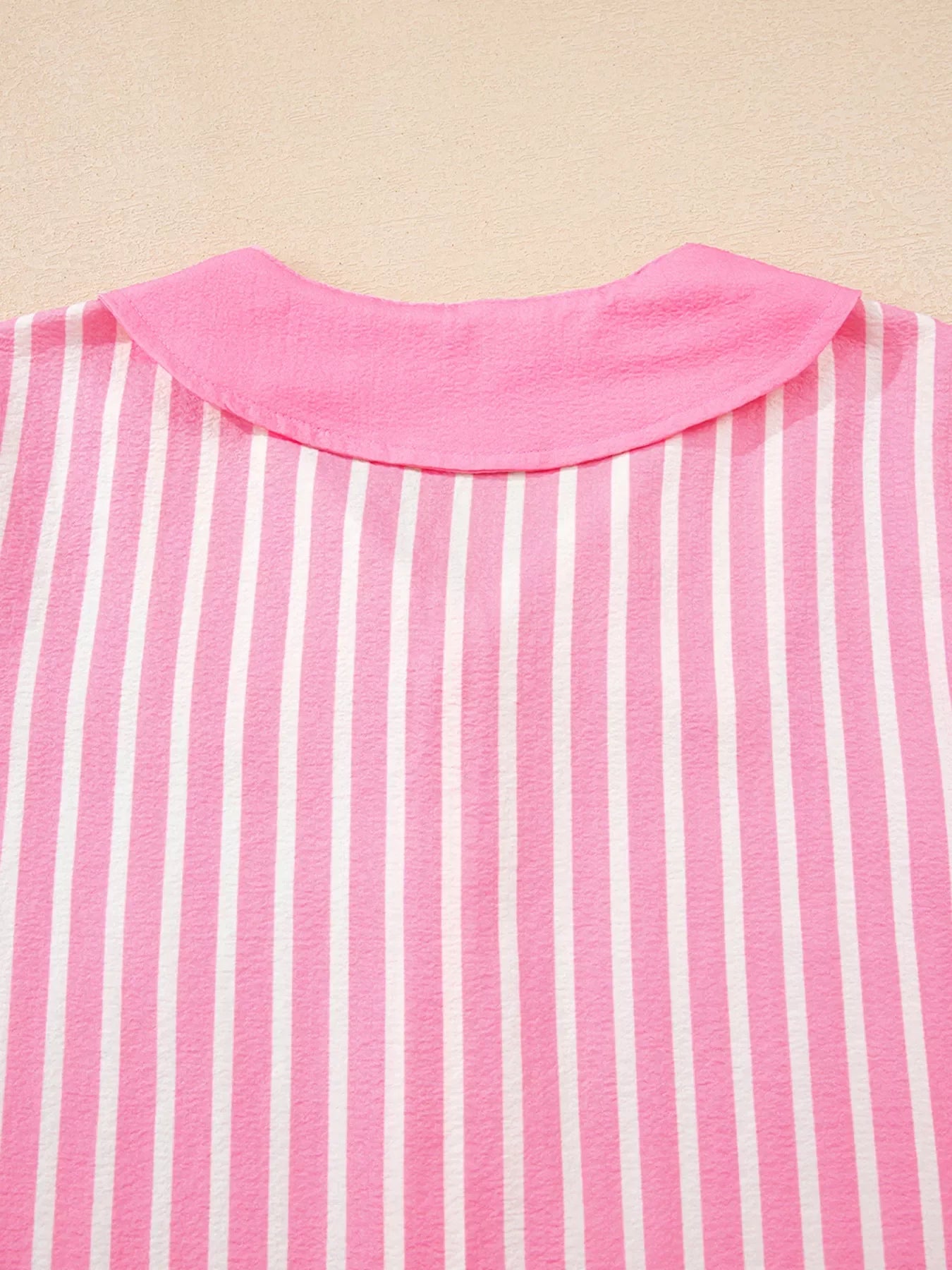 Pink and white vertical striped shirt with a solid pink rounded collar on textured beige background