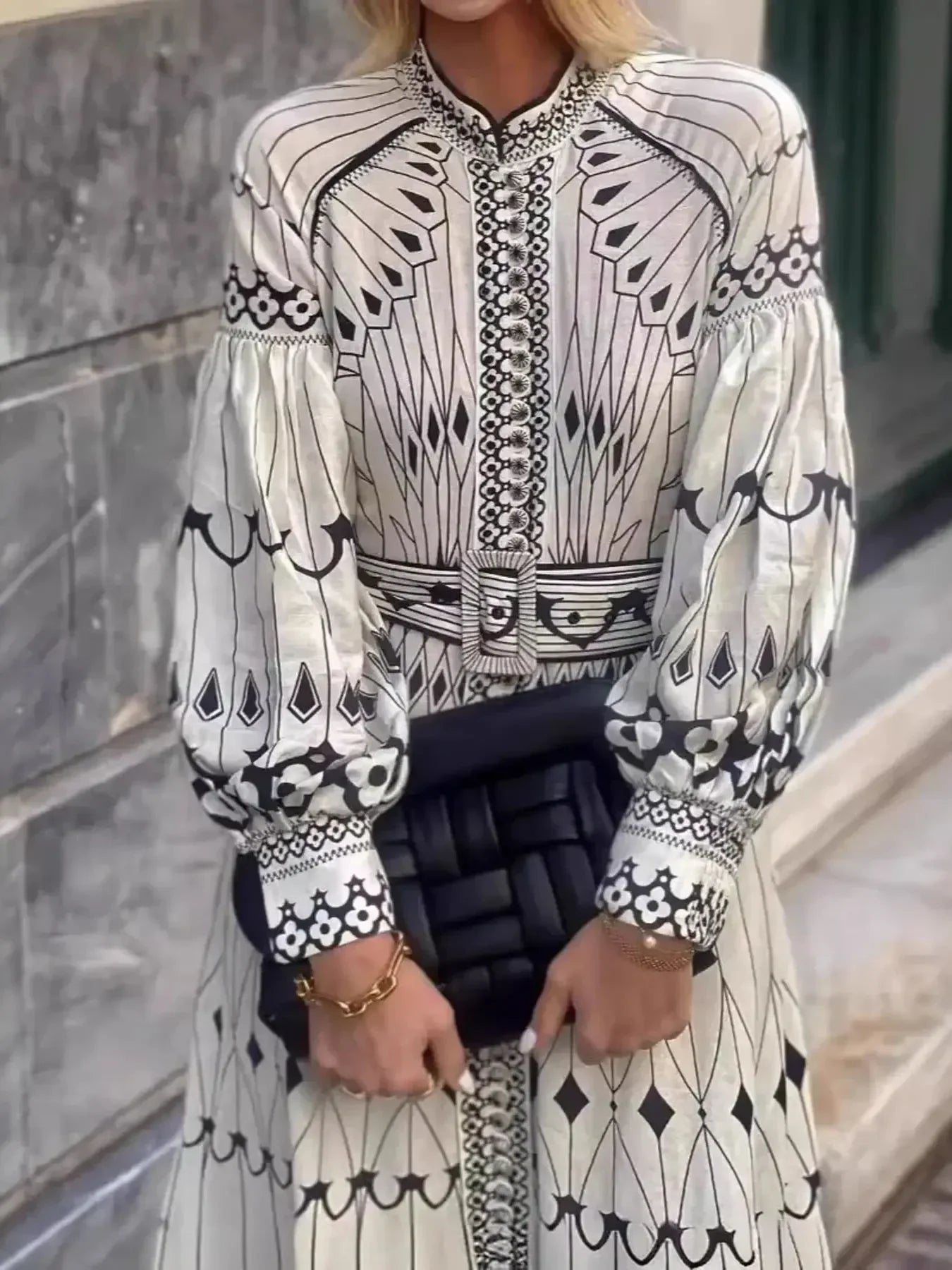 Woman in black and white long-sleeve patterned dress holding black woven clutch bag