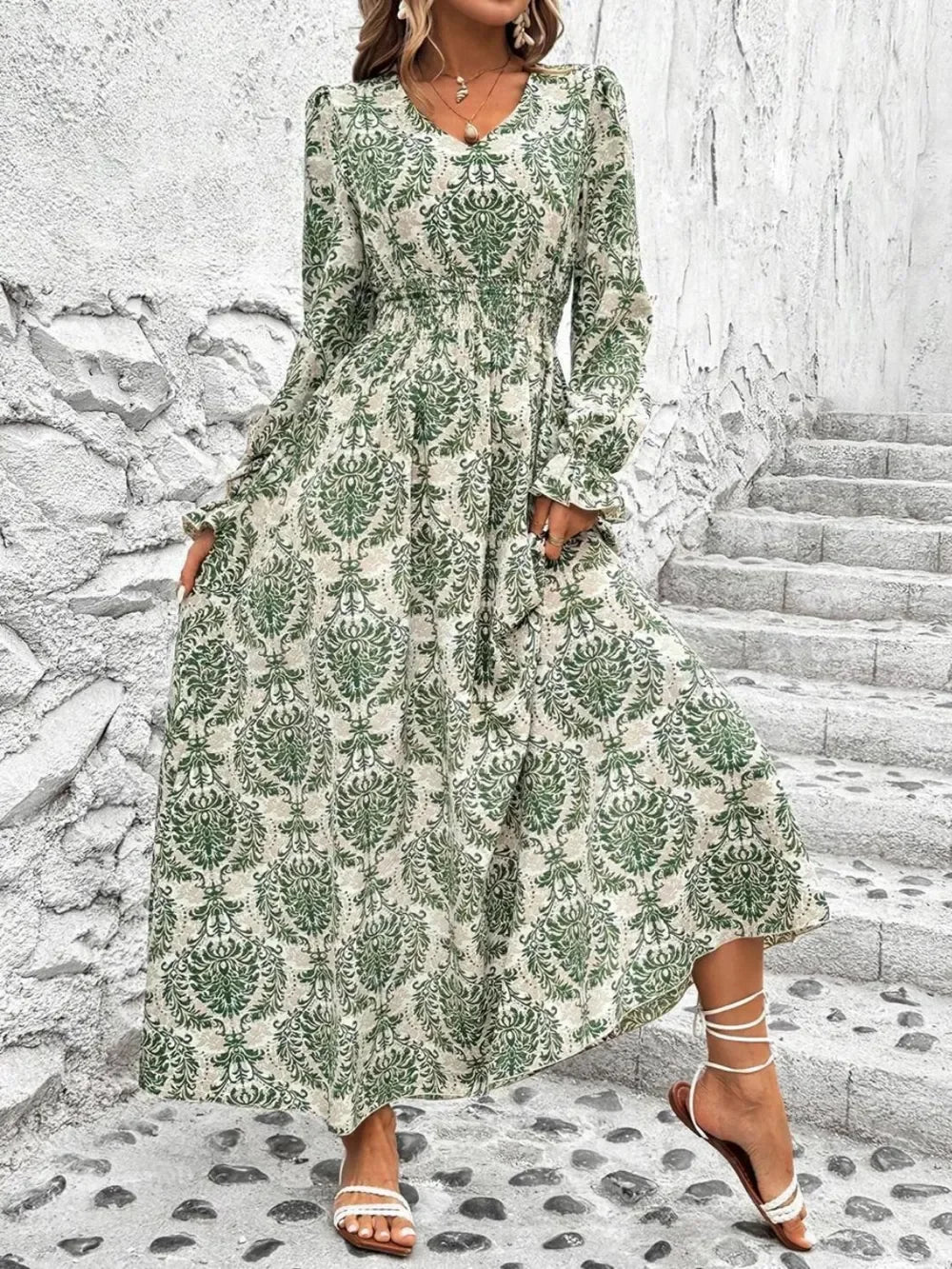 Woman in green and white patterned long sleeve maxi dress with ankle-tie sandals on stone stairs