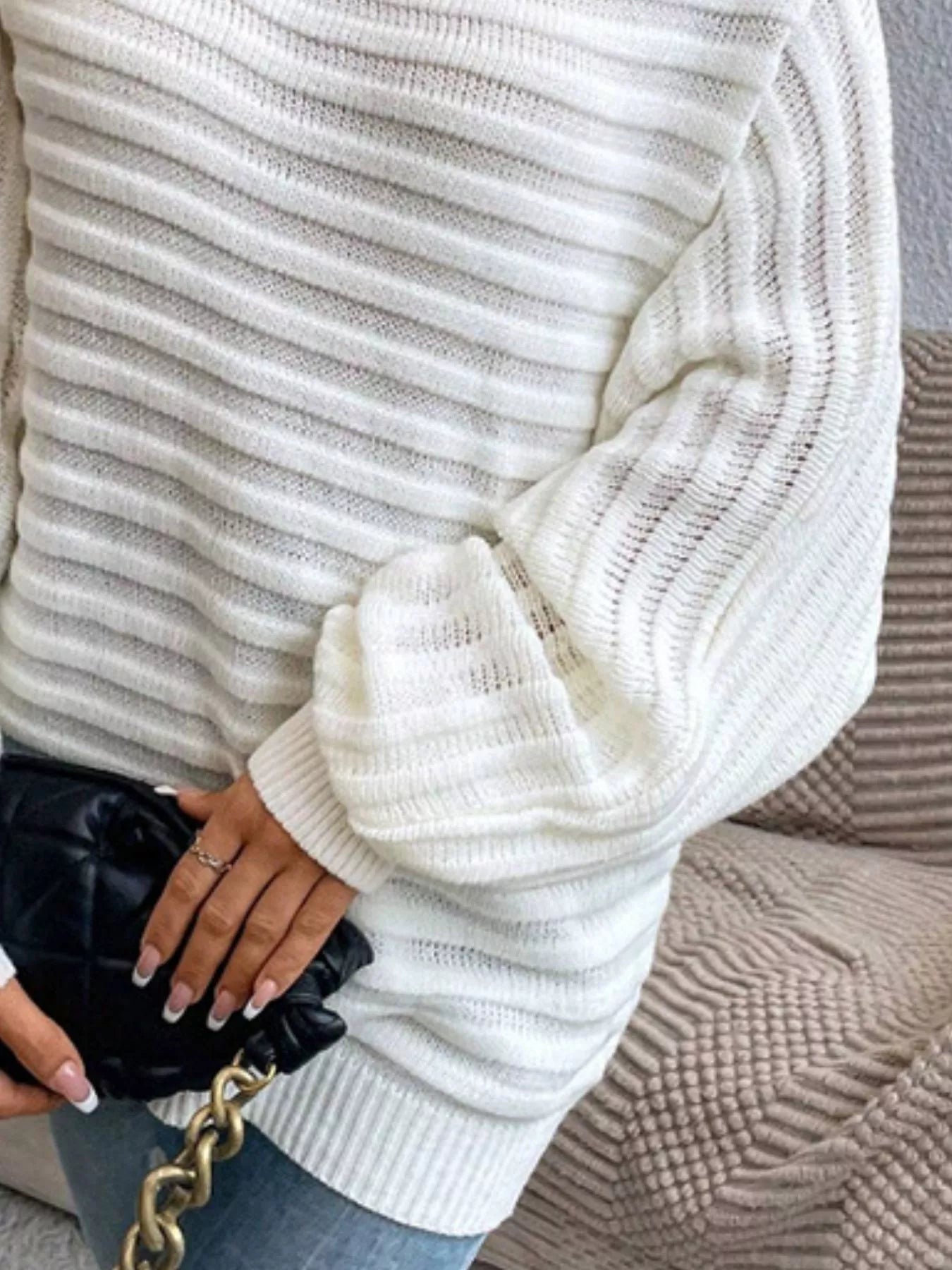 Woman wearing a white ribbed knit oversized sweater and holding a black quilted bag