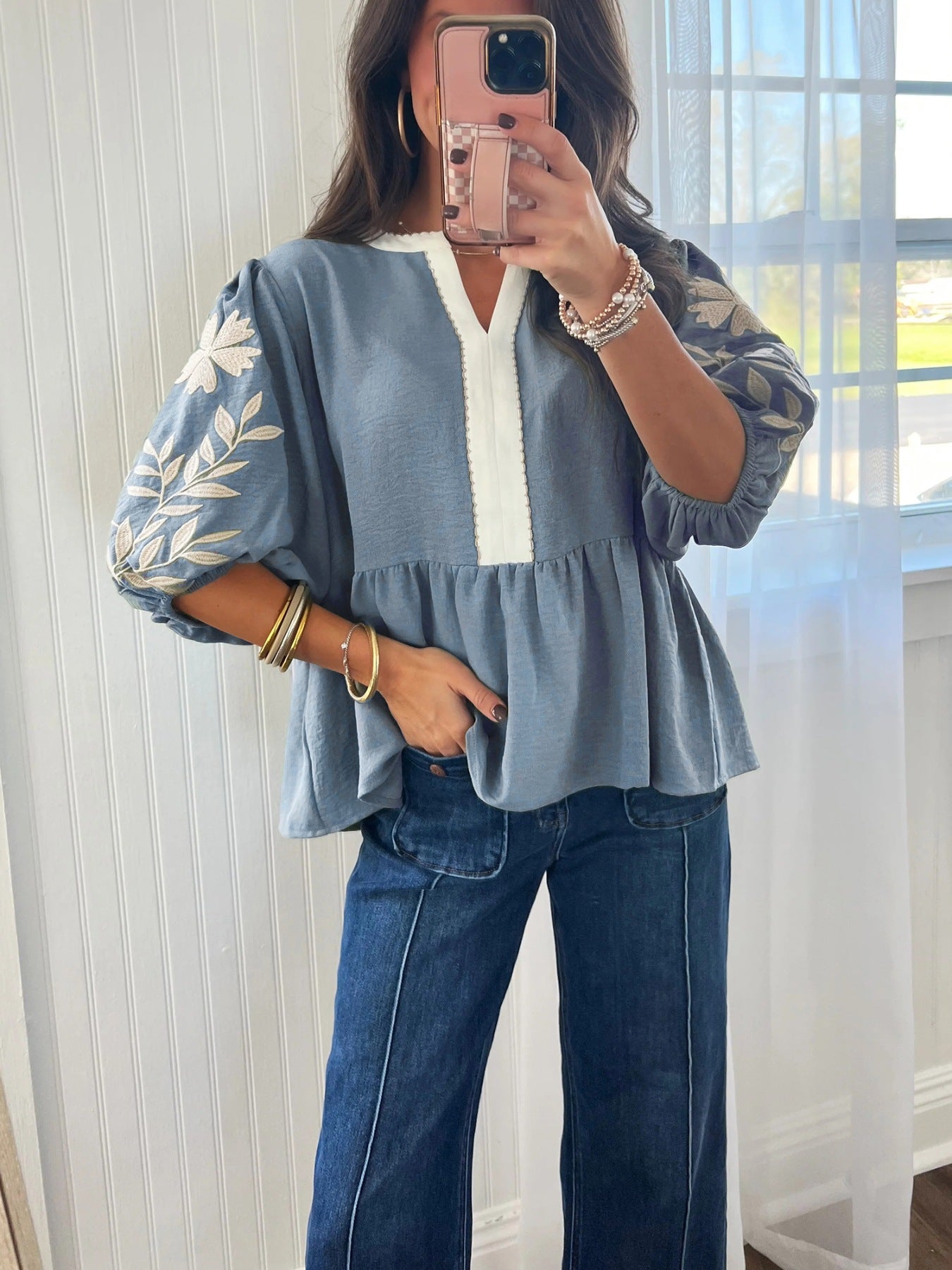 Blue embroidered blouse with white trim, puff sleeves, and peplum hem paired with wide-leg jeans