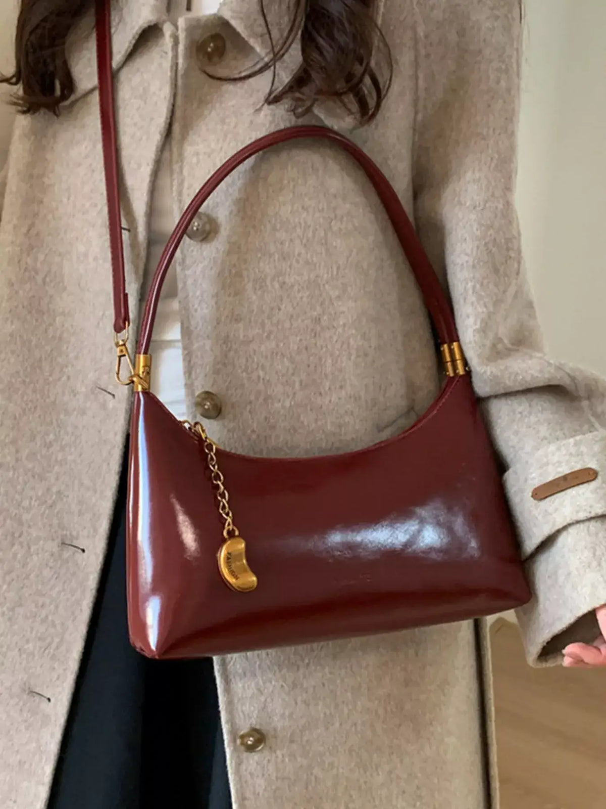 Evie's Dreamland burgundy PU leather shoulder bag with a gold chain charm, paired with a beige wool coat.
