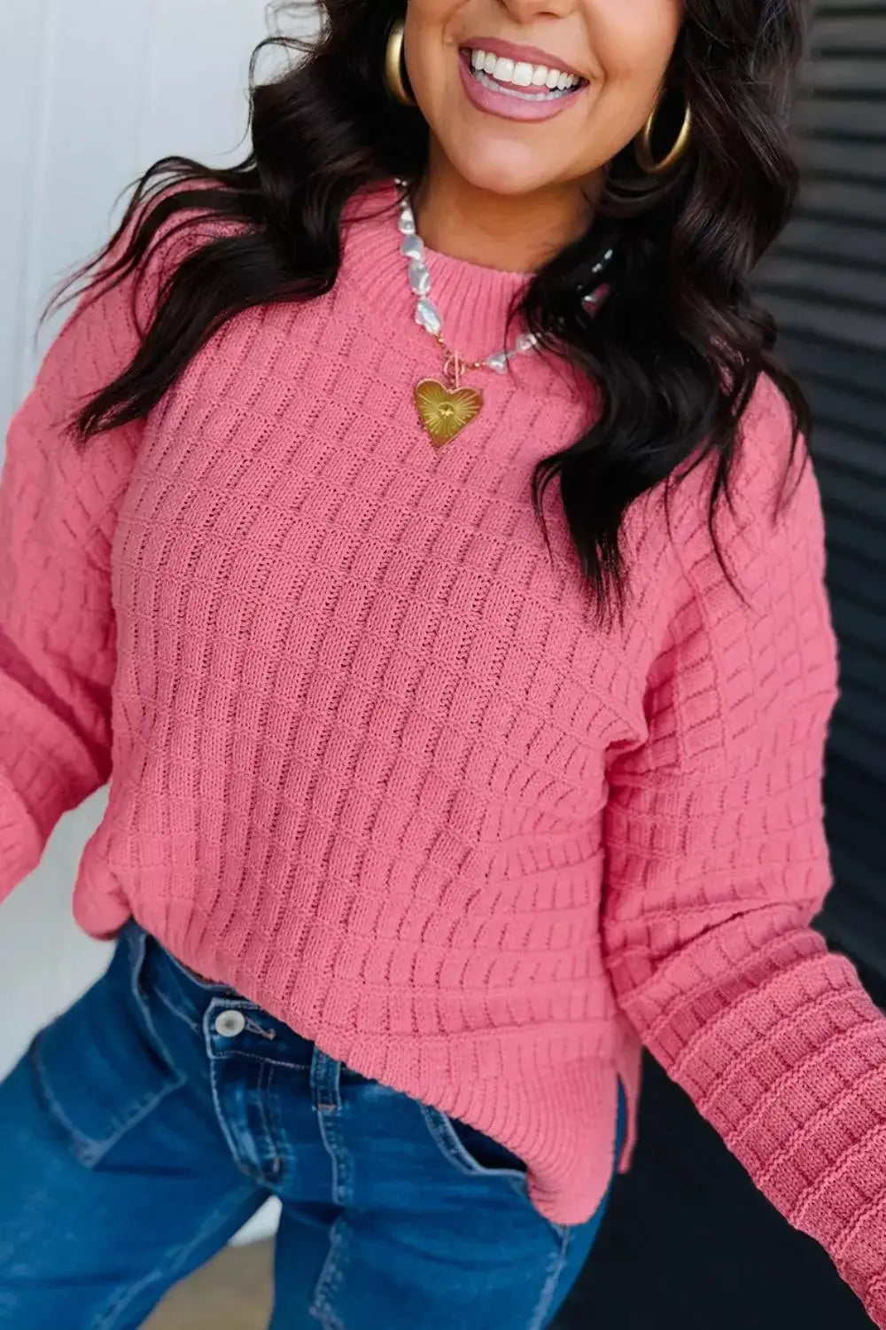 Woman wearing a pink drop shoulder knit sweater by Evie's Dreamland with a heart pendant necklace.
