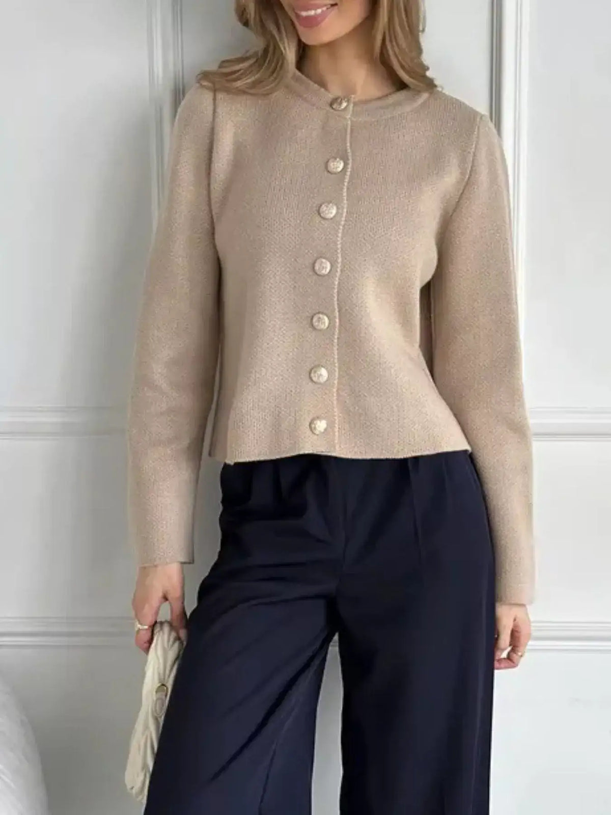 Woman wearing a beige crew neck button down cardigan by Evie's Dreamland paired with navy trousers.