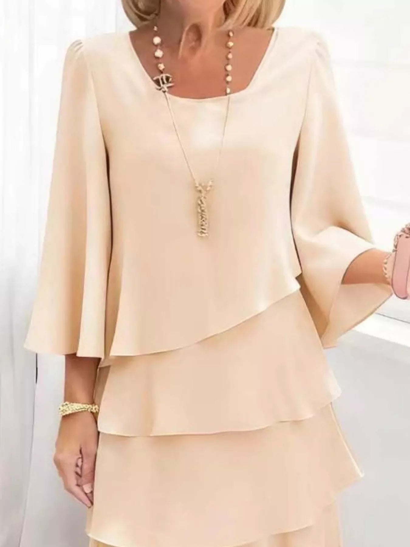 Elegant beige ruffled blouse with bell sleeves, layered tiers, and gold jewelry for chic everyday style