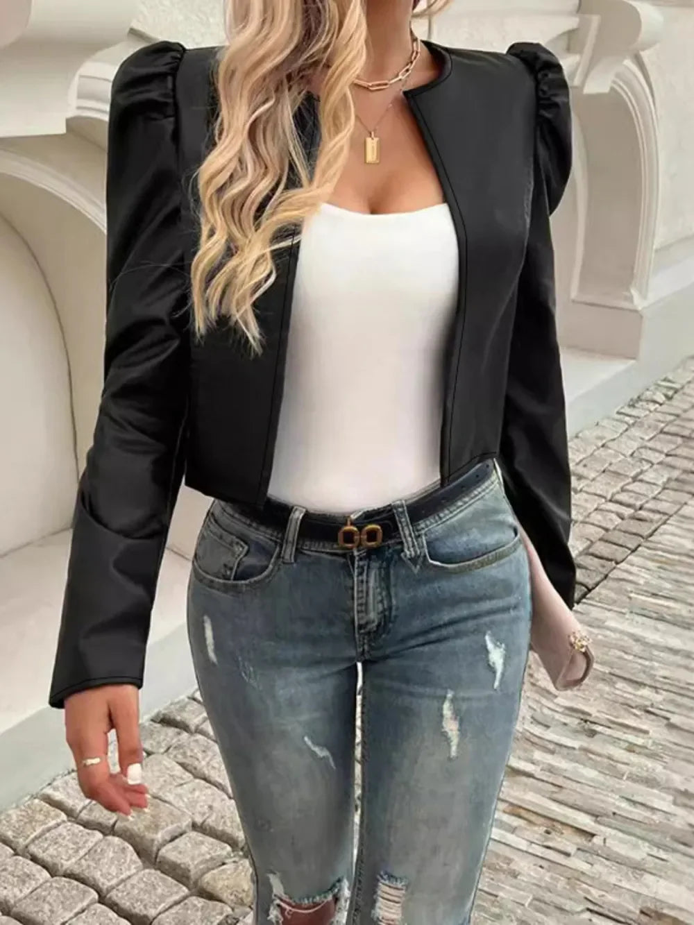 Woman wearing a cropped black puff-sleeve jacket, white top, and distressed blue jeans.