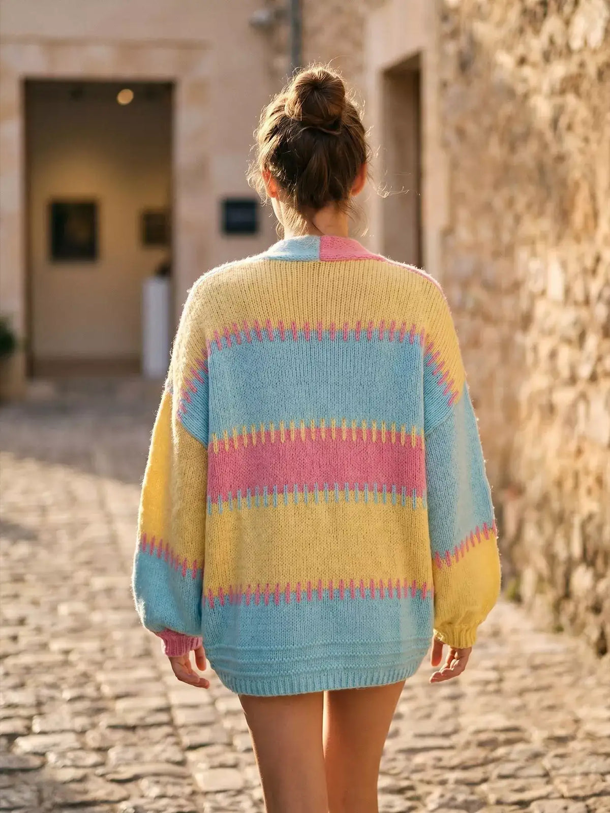 Back view of a woman wearing an Evie's Dreamland color-block V-neck cardigan in pastel yellow, pink, and blue.