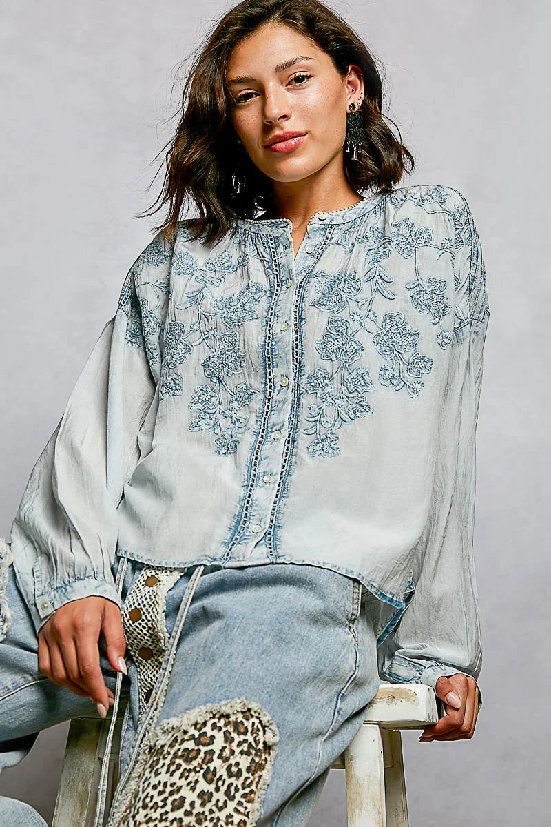 Woman wearing a light blue embroidered blouse with floral pattern and relaxed blue jeans.
