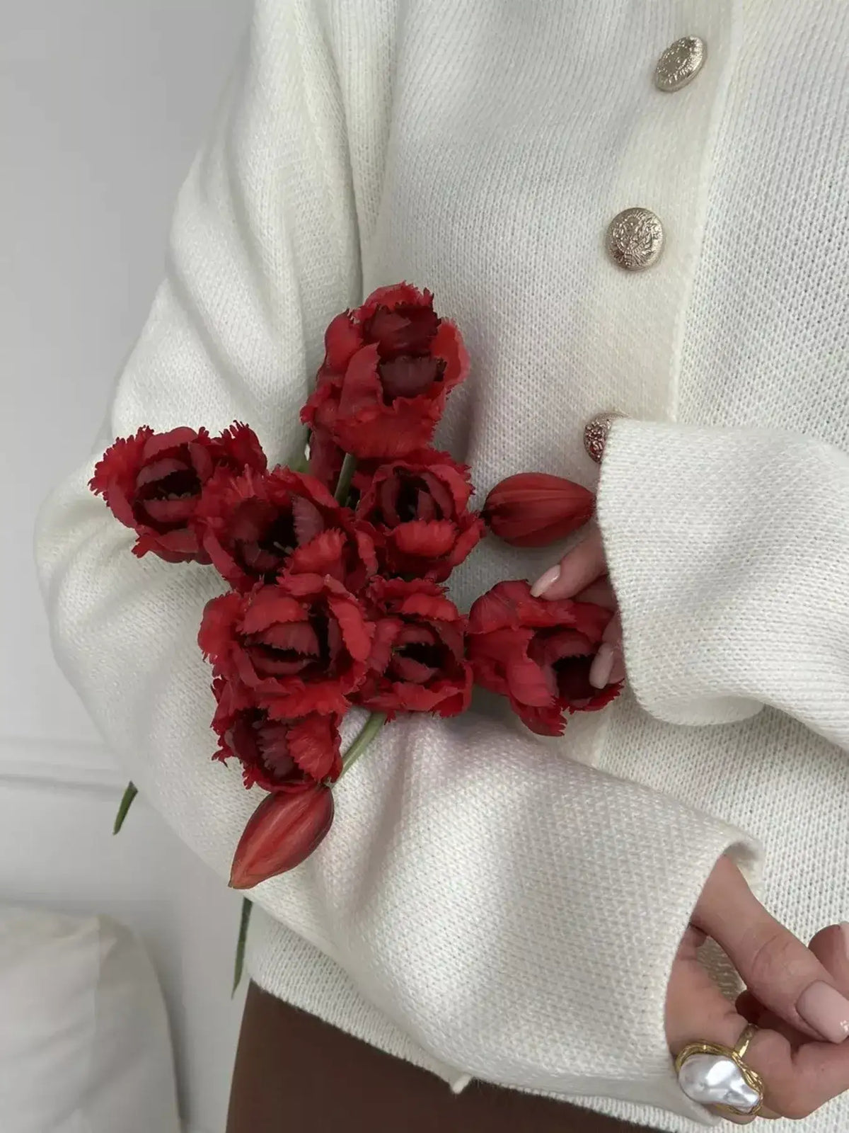 Woman wearing a white Evie's Dreamland crew neck button down cardigan holding red tulips.