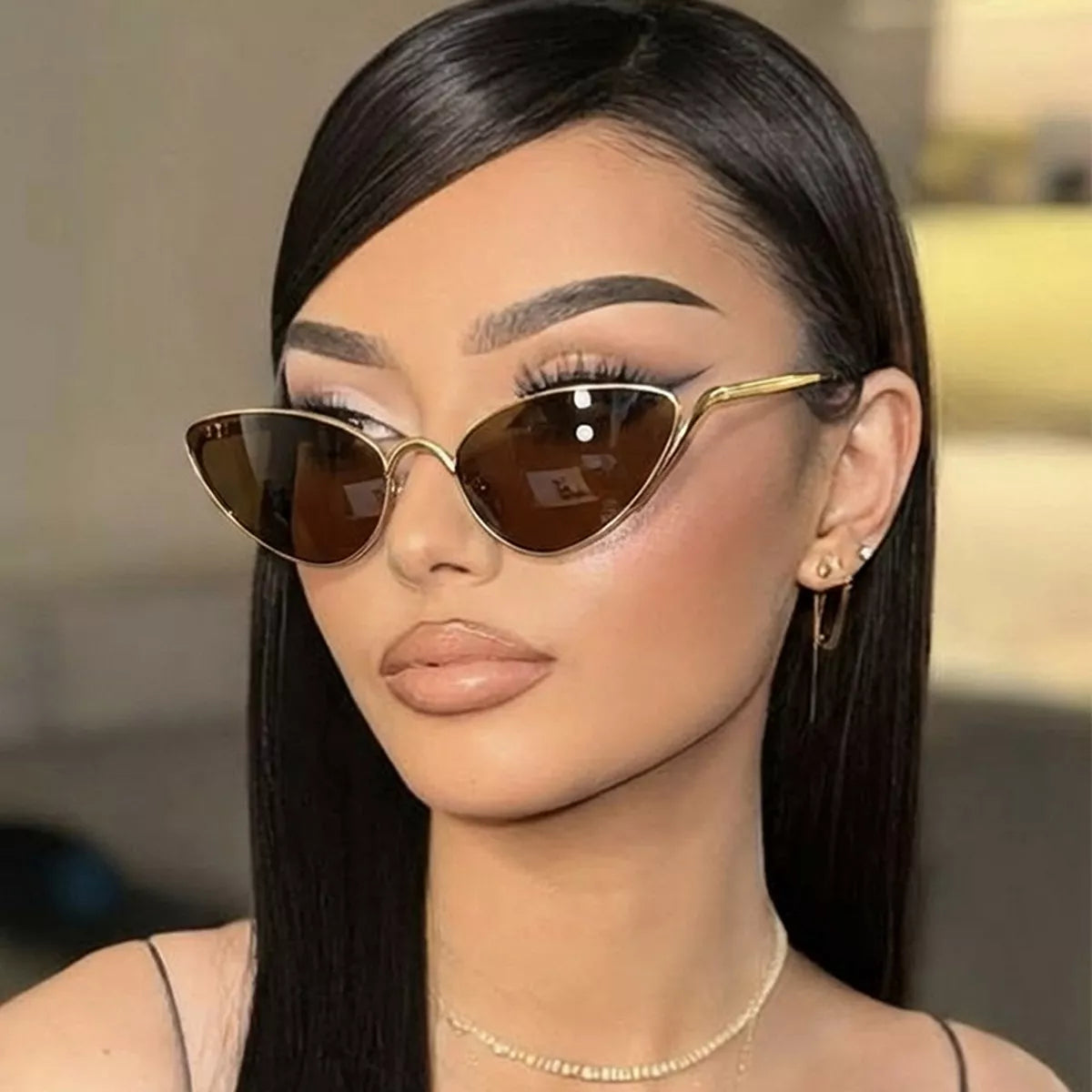 Woman wearing gold-framed cat-eye sunglasses and a delicate gold necklace.