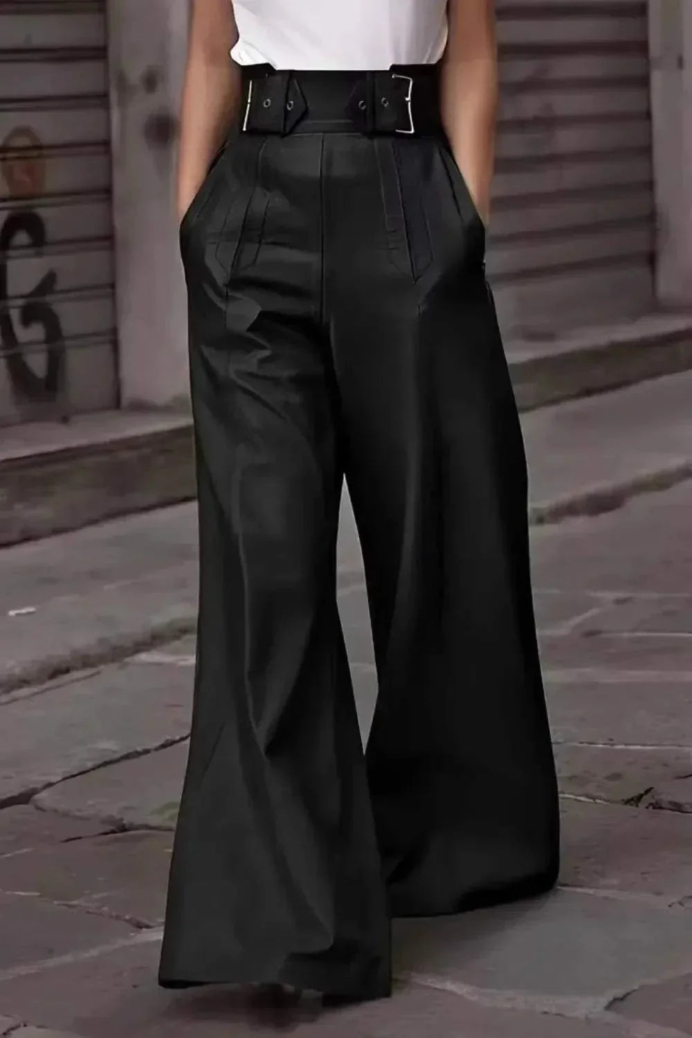 Woman wearing high-waisted, wide-leg black pants with belt and white top on urban sidewalk