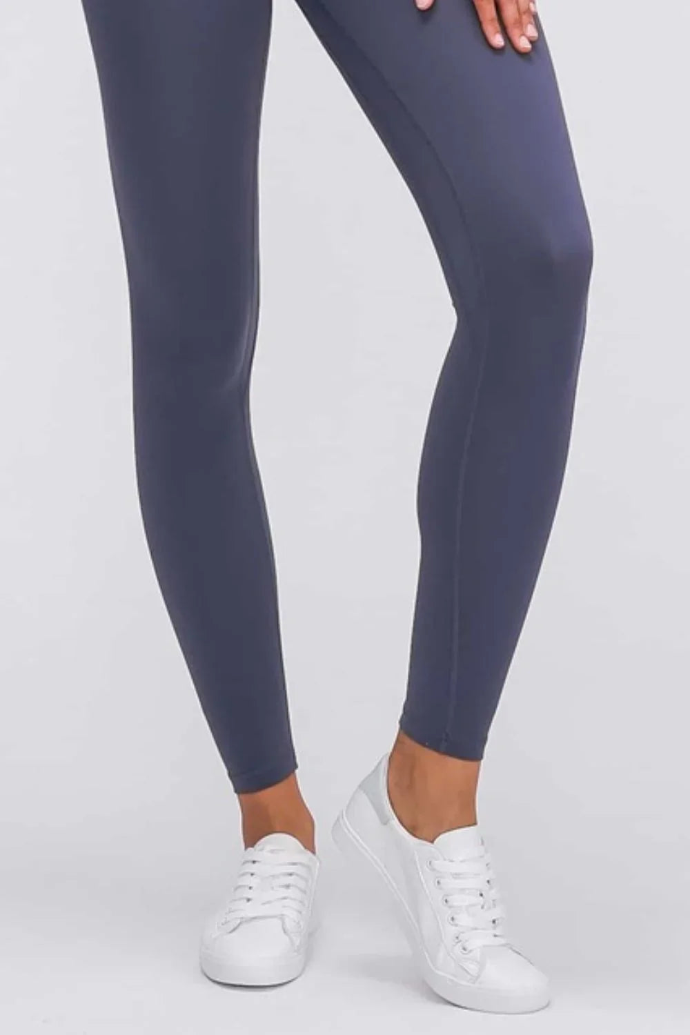 Close-up of a person wearing dark gray leggings and white sneakers on a plain background