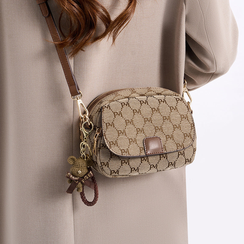 Woman wearing a beige patterned crossbody bag with brown leather strap and bear keychain.