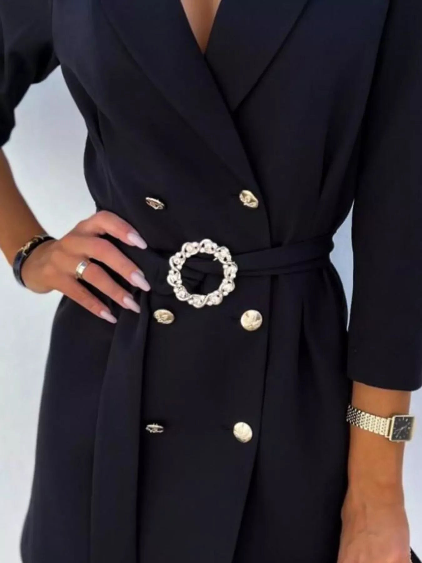 Woman wearing a black belted coat dress with gold buttons and a decorative circular belt buckle