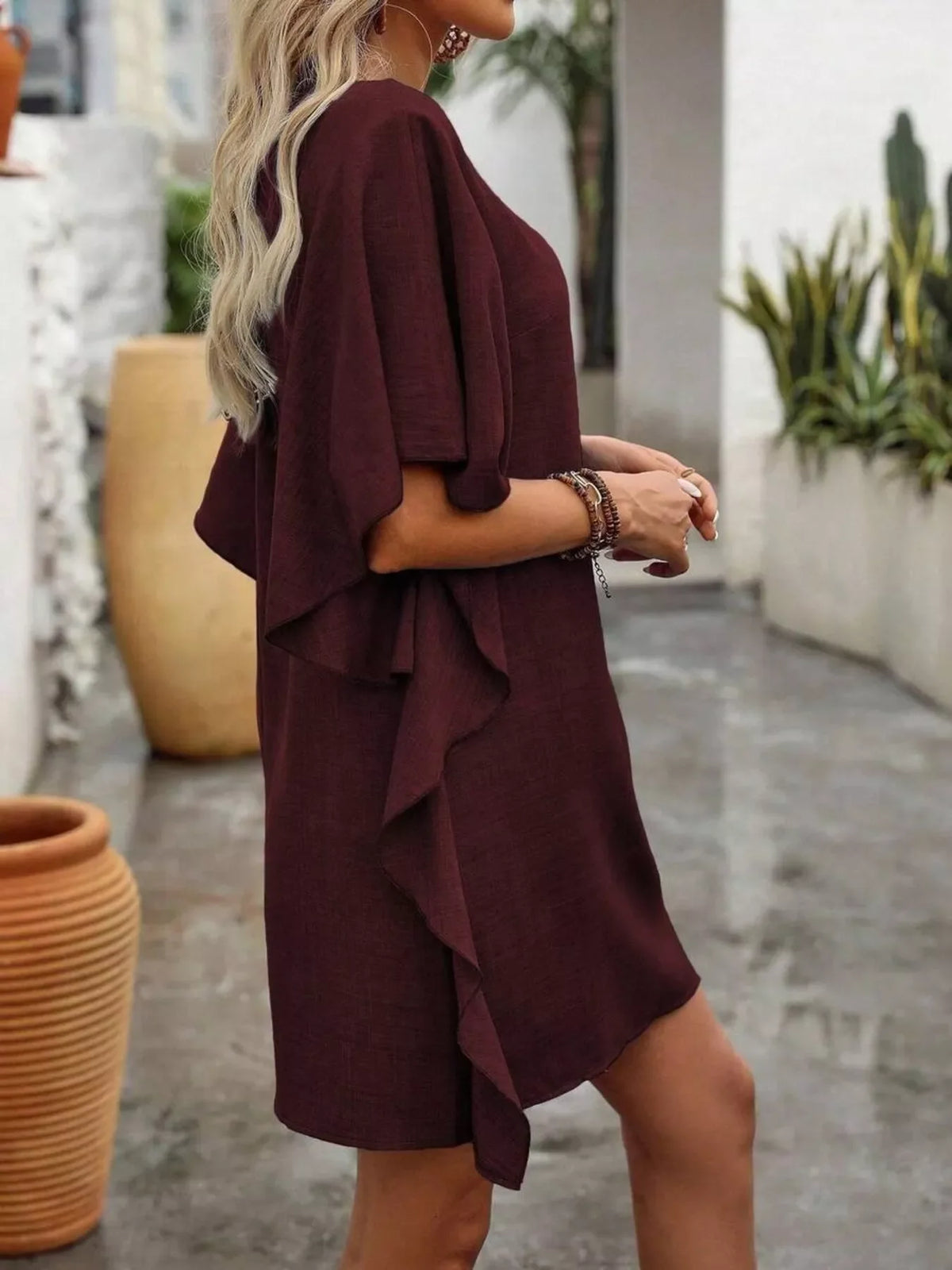 Woman wearing a short-sleeve burgundy ruffle dress, outdoor scene with potted plants.