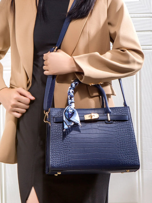 Woman in tan blazer holding navy blue crocodile-embossed handbag with silk scarf accent