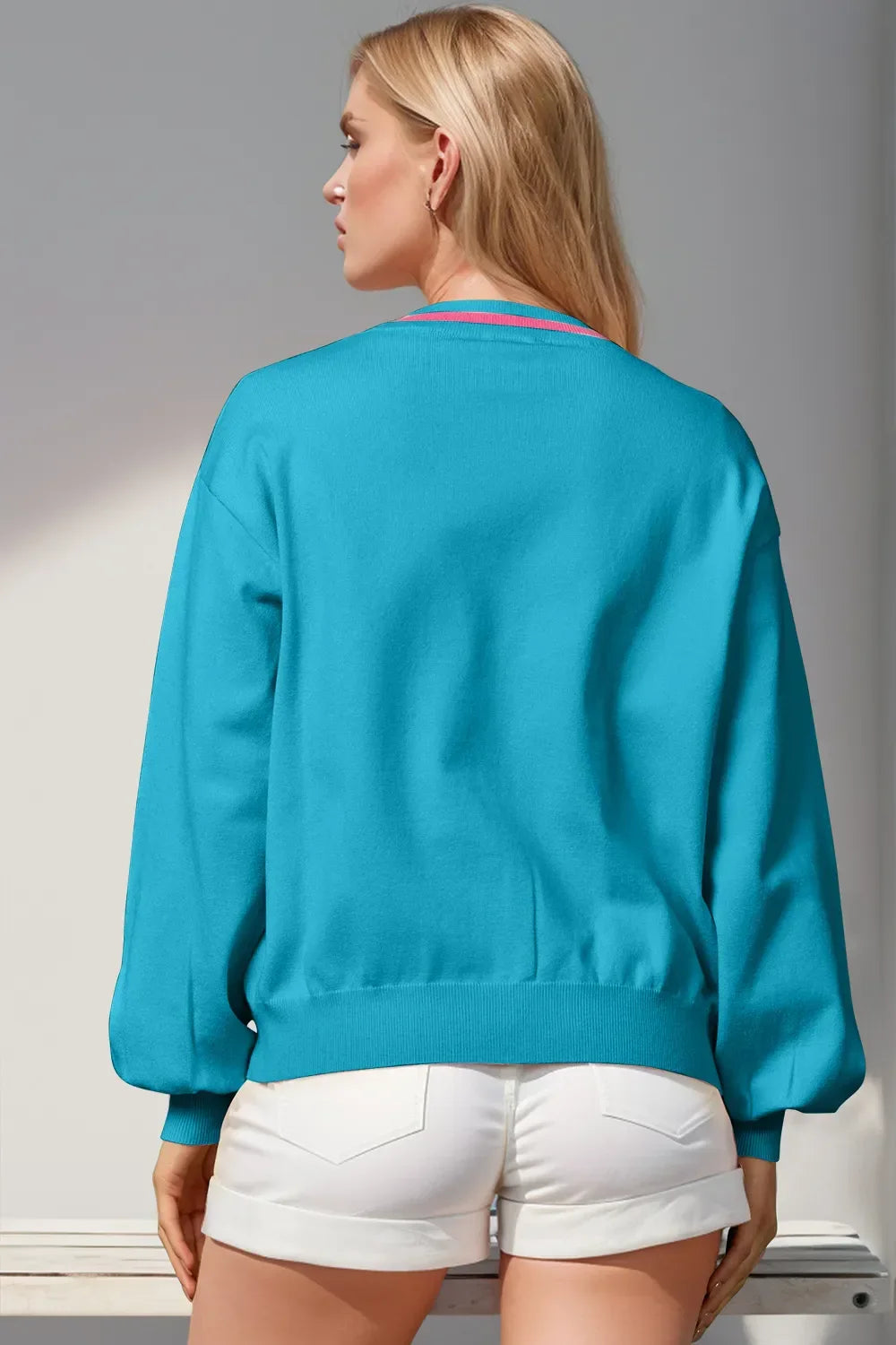 Woman wearing a bright blue long-sleeve sweater and white rolled-up shorts, standing with back to camera