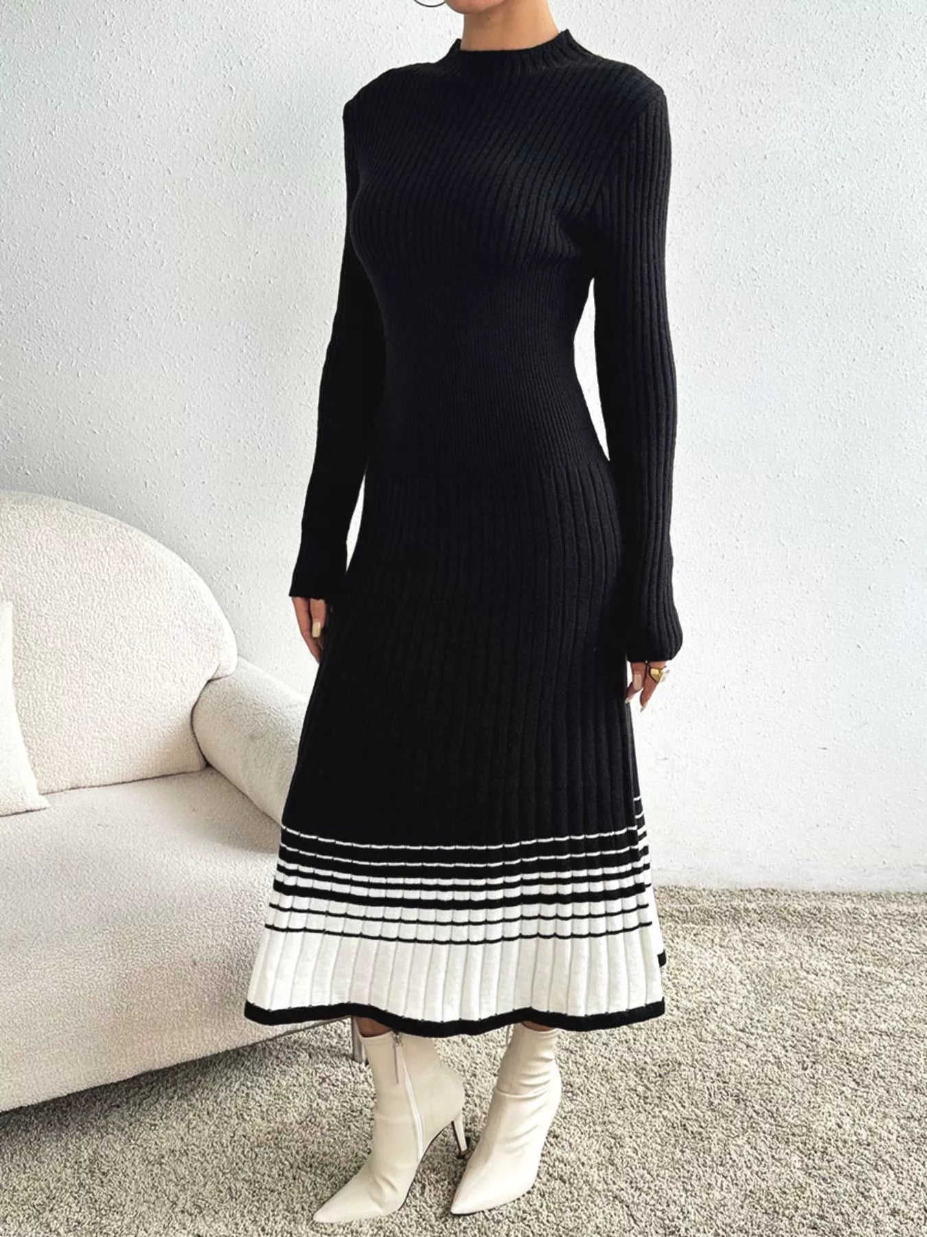 Woman wearing a black ribbed knit midi dress with a white striped hem and white ankle boots