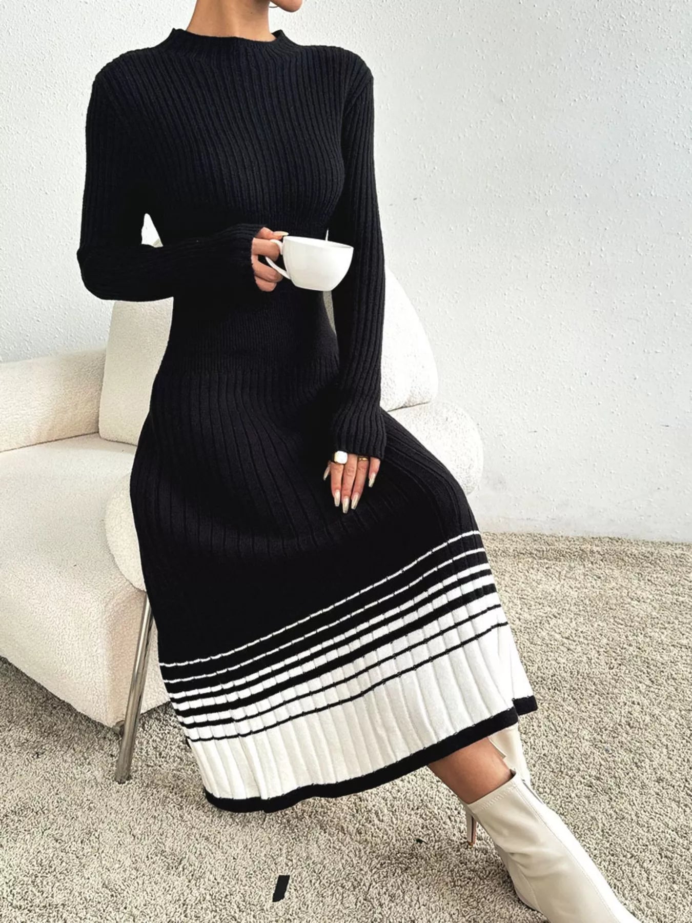 Woman wearing a black ribbed knit midi dress with white striped hem and white boots.