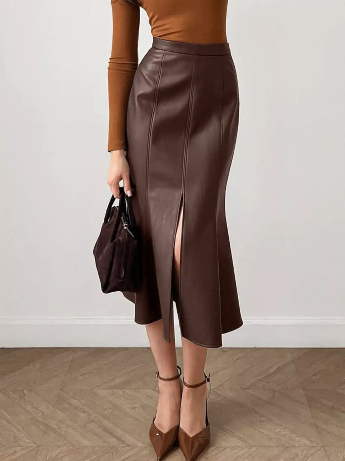 Woman wearing an Evie's Dreamland brown faux leather mermaid midi skirt with a front slit and brown heels.