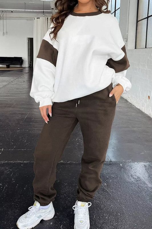 Woman wearing brown and white color block sweatshirt with matching brown joggers and white sneakers in a loft-style room