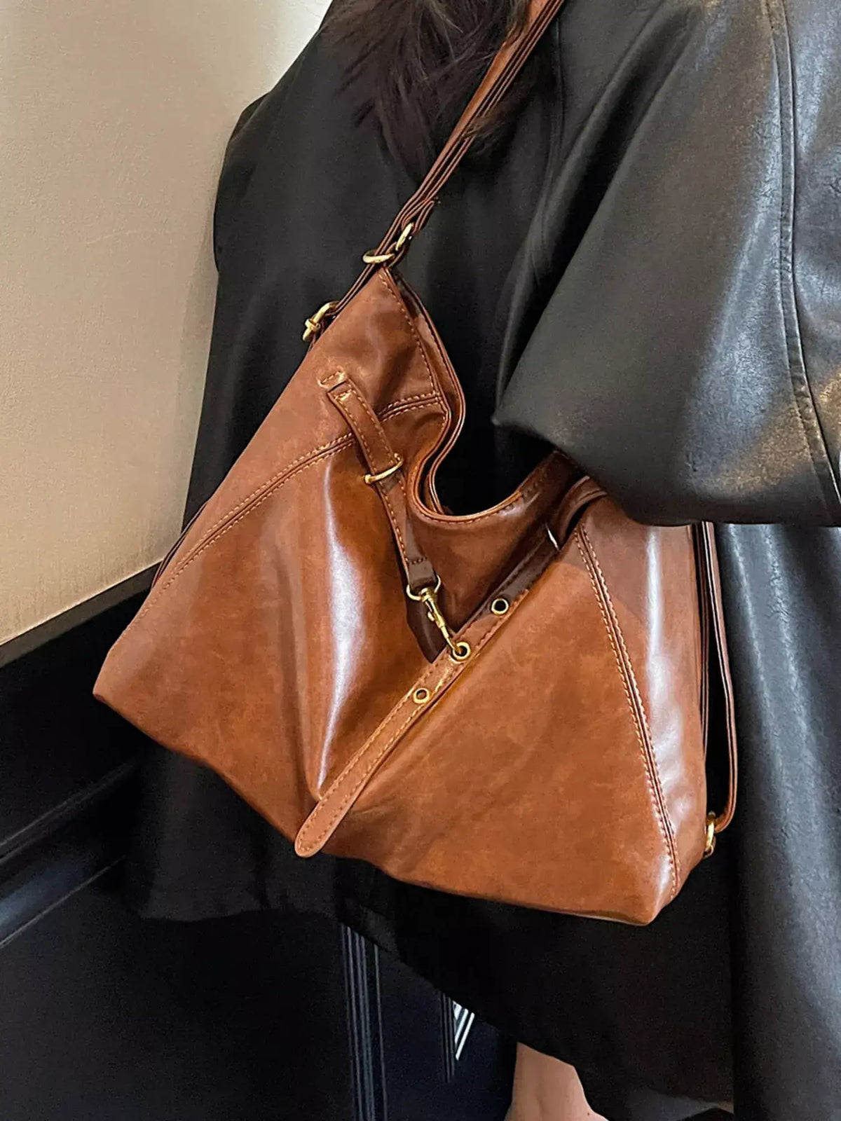 Brown vintage style PU leather crossbody bag with gold-tone hardware worn over a black jacket.