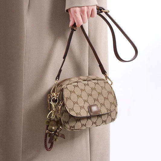 Woman holding a stylish beige crossbody bag with brown monogram print and bear keychain