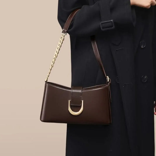 Brown PU leather shoulder bag with gold chain strap and buckle, worn over a black coat