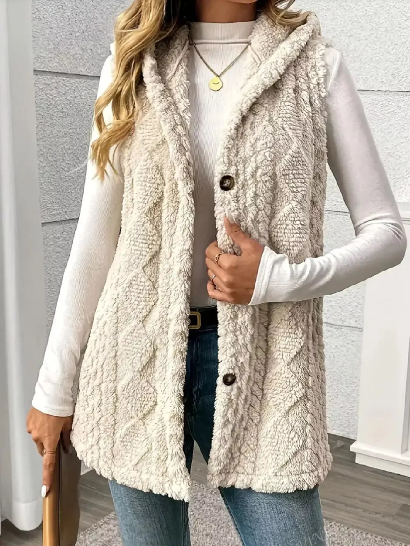 Woman wearing a cozy beige sherpa fleece vest over white long sleeve shirt and blue jeans