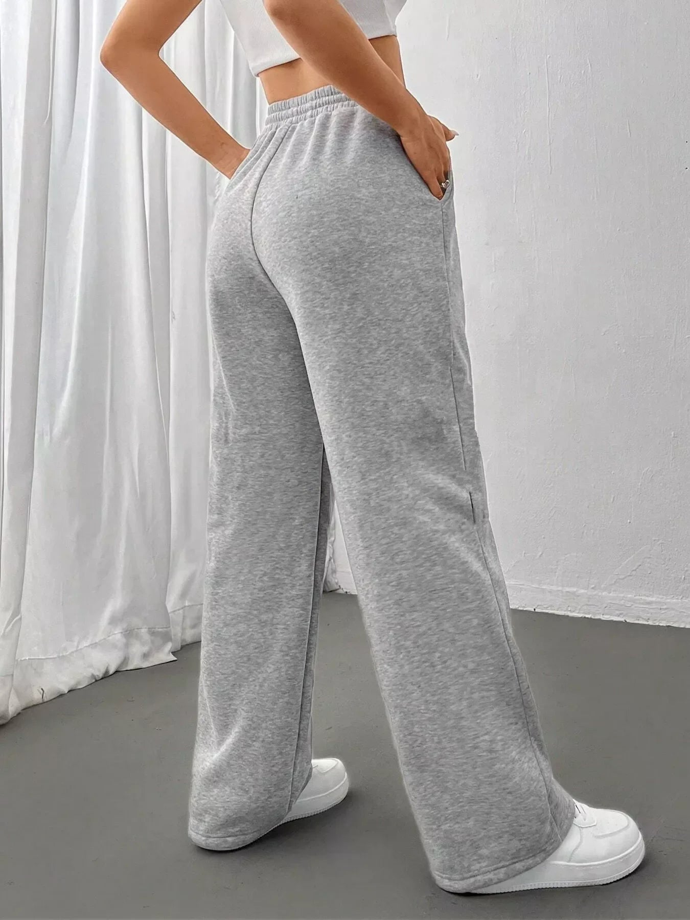 Woman wearing light gray wide-leg sweatpants with elastic waist and white sneakers indoors