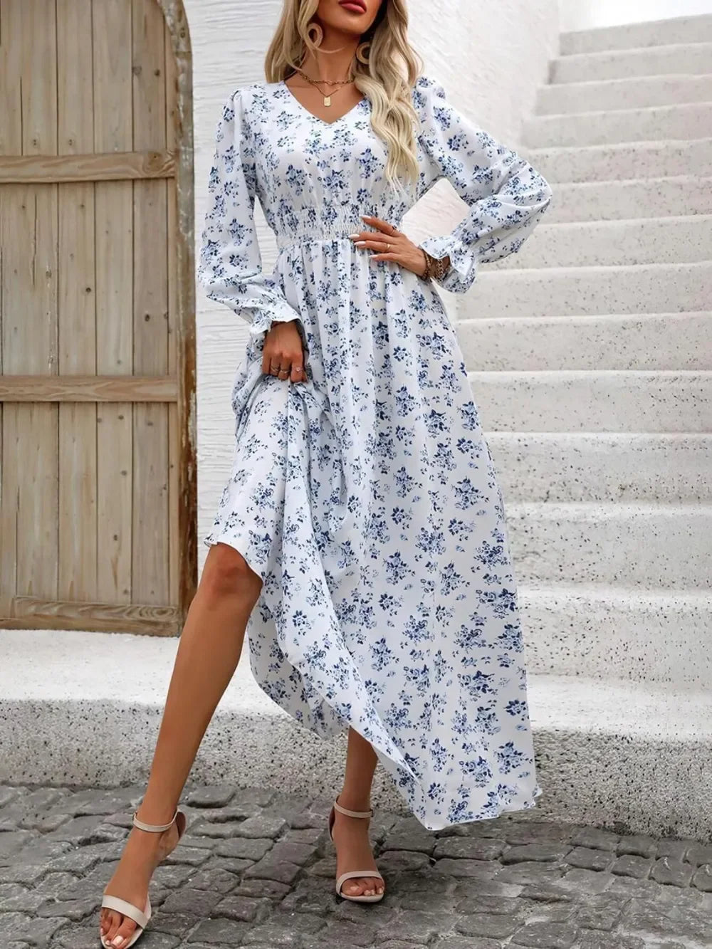 Woman wearing white floral long-sleeve maxi dress with blue flowers and beige sandals on stone steps