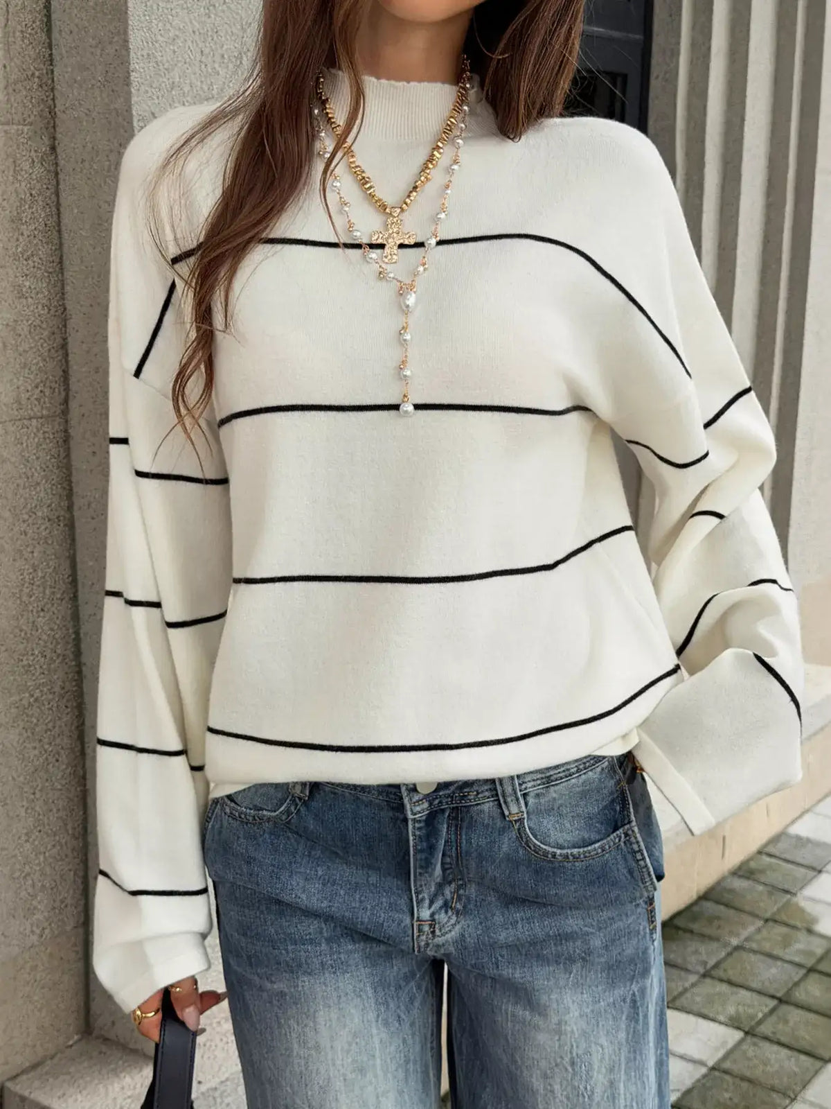 Woman wearing an Evie's Dreamland white mock neck knit sweater with black stripes and blue jeans.