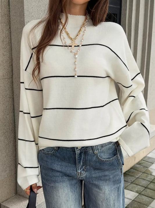Woman wearing an Evie's Dreamland white mock neck knit sweater with black stripes and blue jeans.