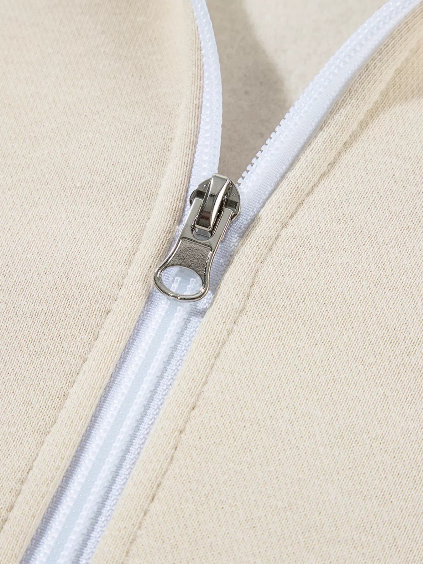 Close-up of silver zipper on beige fabric with white zipper tape and visible stitching